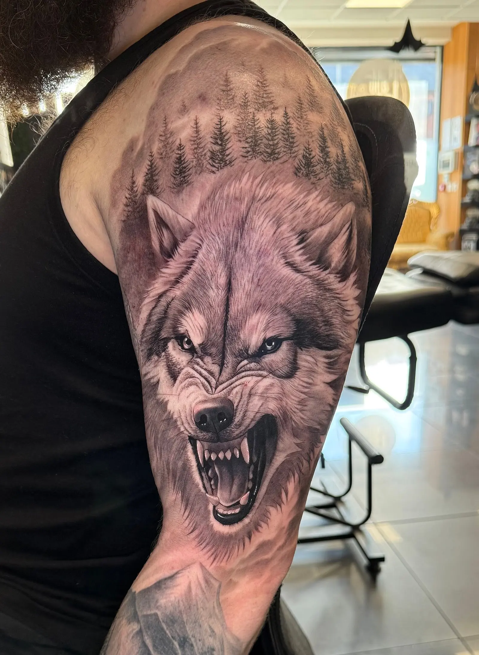 Tatouage réaliste noir et gris d'une tête de loup sur l'épaule