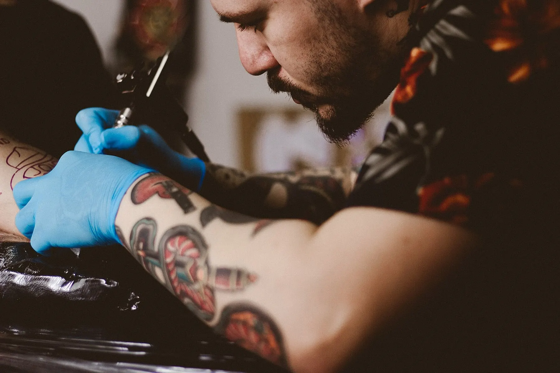 Tatoueur en pleine séance, gants et machine à tatouer, au studio Noir d'Encre à Agen